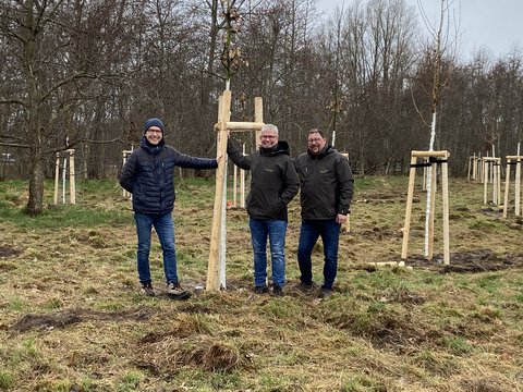 Jens Bagehorn-Delor, Stadt Schleswig, Öffentliches Grün sowie Sven Schnoor und Sven Hörmann, Firma Schnoor Garten- und Landschaftsbau, Schuby stehen vor einer Baumgruppe