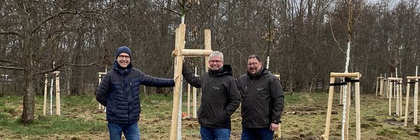 Jens Bagehorn-Delor, Stadt Schleswig, Öffentliches Grün sowie Sven Schnoor und Sven Hörmann, Firma Schnoor Garten- und Landschaftsbau, Schuby stehen vor einer Baumgruppe