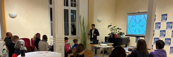 Frank Martis im Vordergrund erklärt den Teilnehmenden das Demokratiespiel Quararo auf einem Bildschirm im Hintergrund