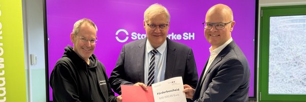 Übergabe Fördermittelbescheid: Bernd Reichelt (Stadtwerke SH), Bürgermeister Stephan Dose und Umweltminister des Landes Schleswig-Holstein, Tobias Goldschmidt halten den Fördermittelbescheid in die Kamera