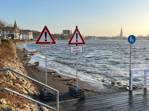 Hochwasser an der Schlei, die Schlei tritt über die Ufer, der Gehweg an der Promenade ist mit Schildern "Achtung, Hochwasser"