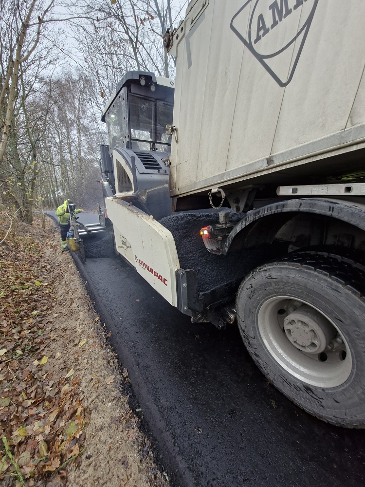 Der Fertiger bringt den Asphalt auf die Trasse auf. Es riecht stark nach Teer und ist sehr warm.
